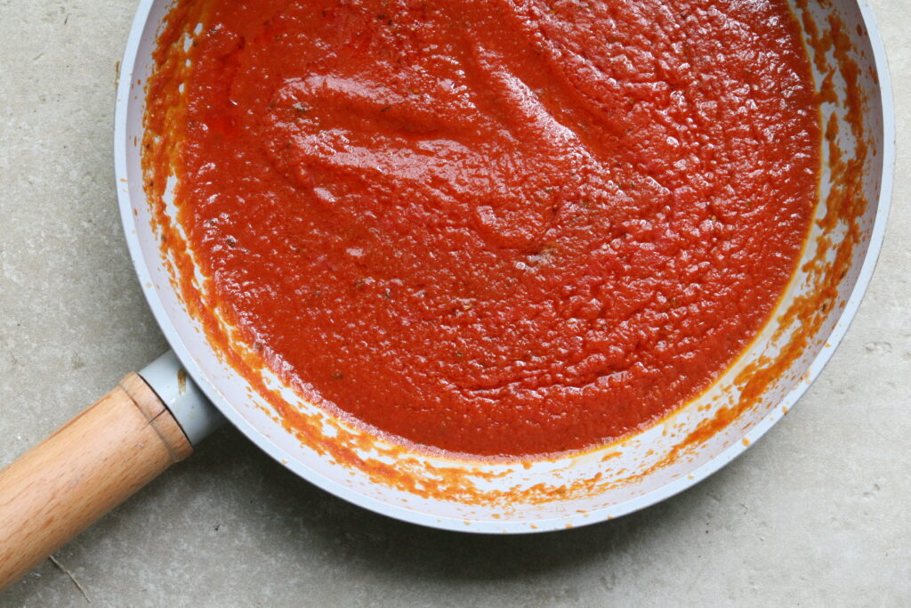 red pizza sauce in a grey frying pan with a wooden handle