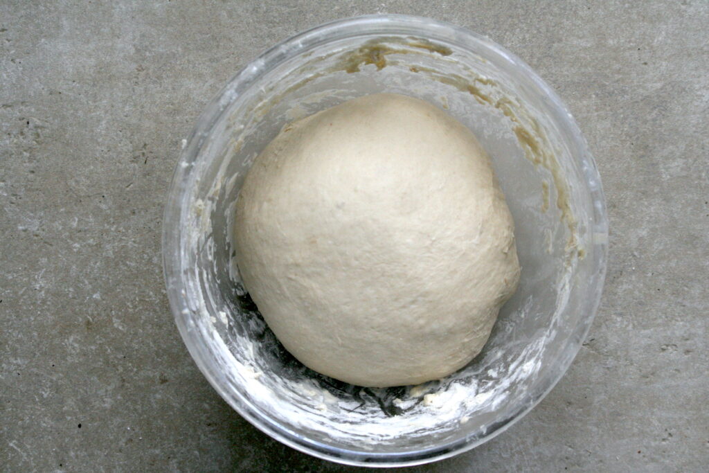 a ball of dough rising in a glass bowl on a grey surface