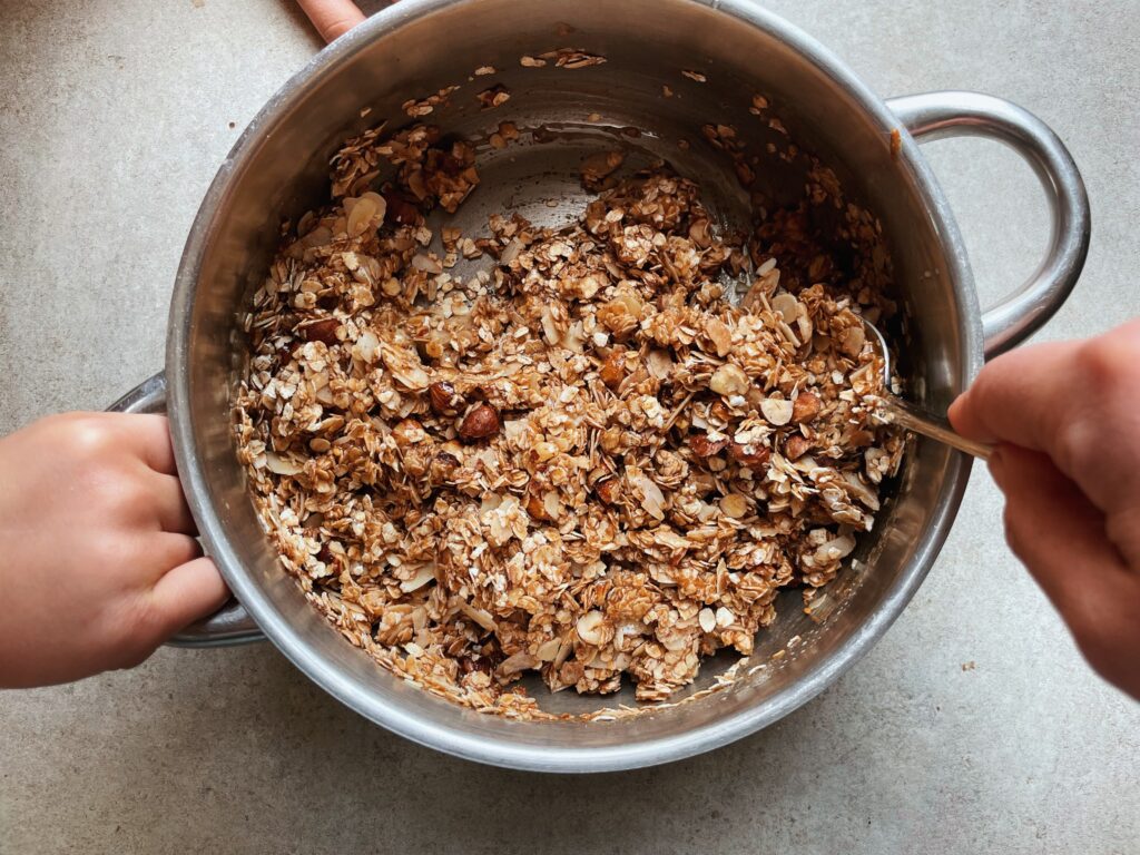 metal saucepan with granola ingredients in it being held by two hands