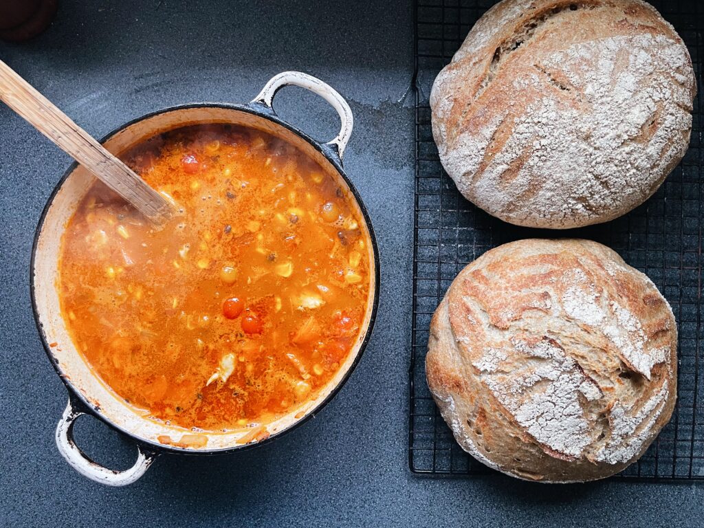 Chicken soup in a white casserole pan with 2 loaves of sourdough.