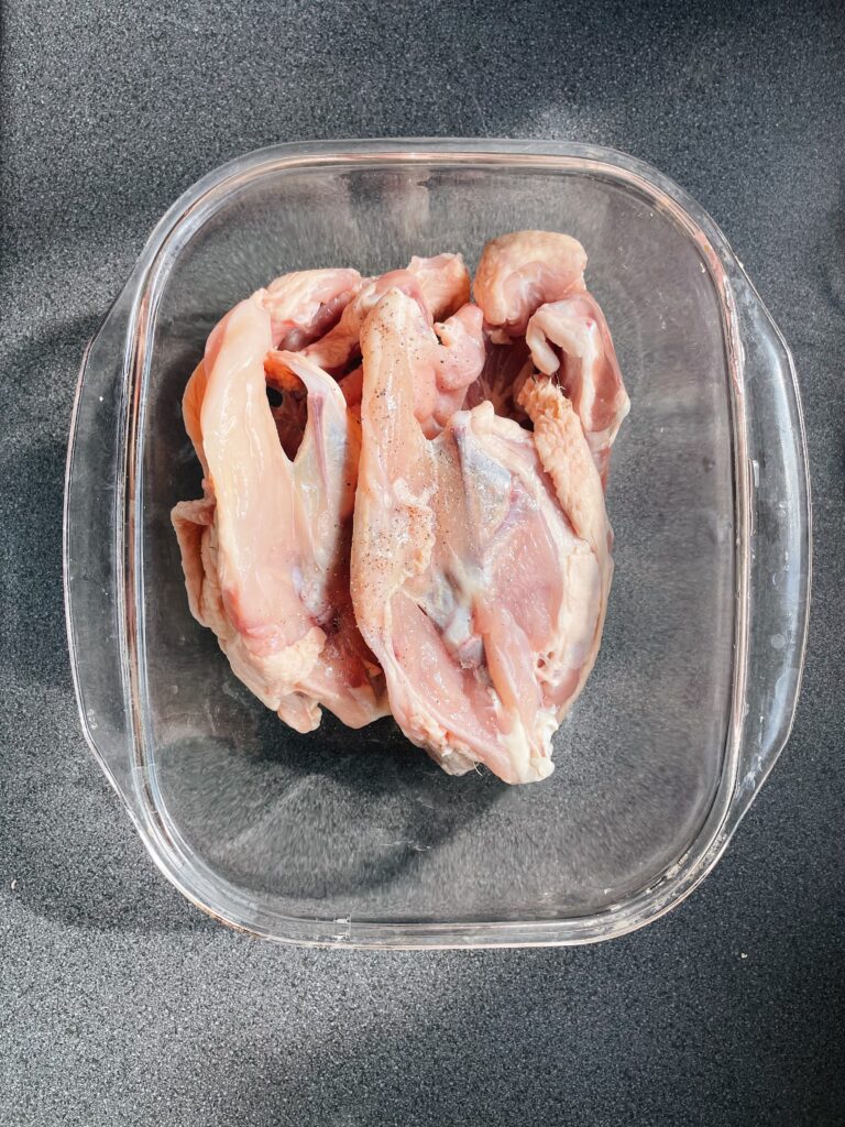 two chicken carcasses in a glass baking dish on a grey counter. top down view.